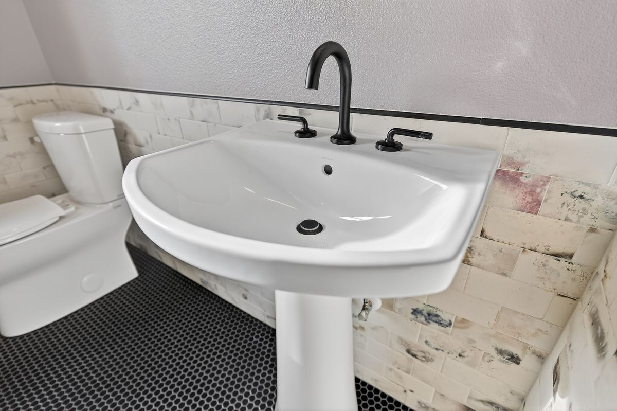 ADU bath with pedestal sink, matte black fixtures and penny-tile floor