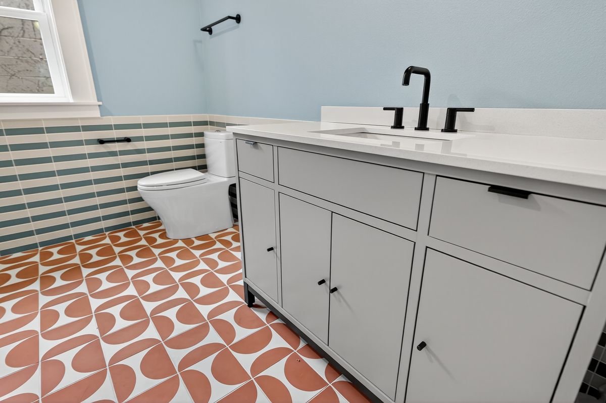 Main bath with terracotta patterned floor tile, striped wall tile and grey vanity