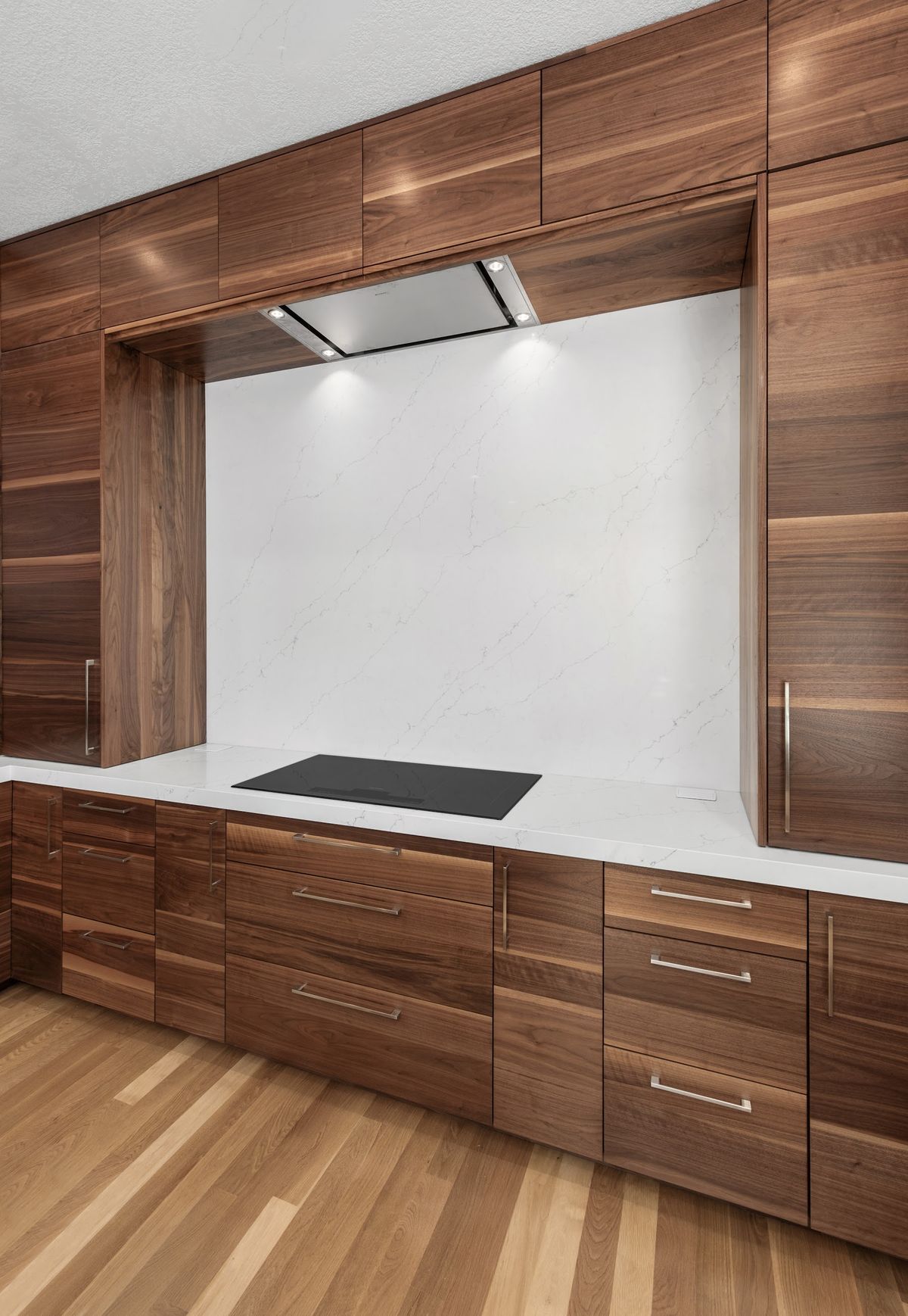 Cooktop wall: full-height quartz backsplash framed in walnut, with the new wall hood