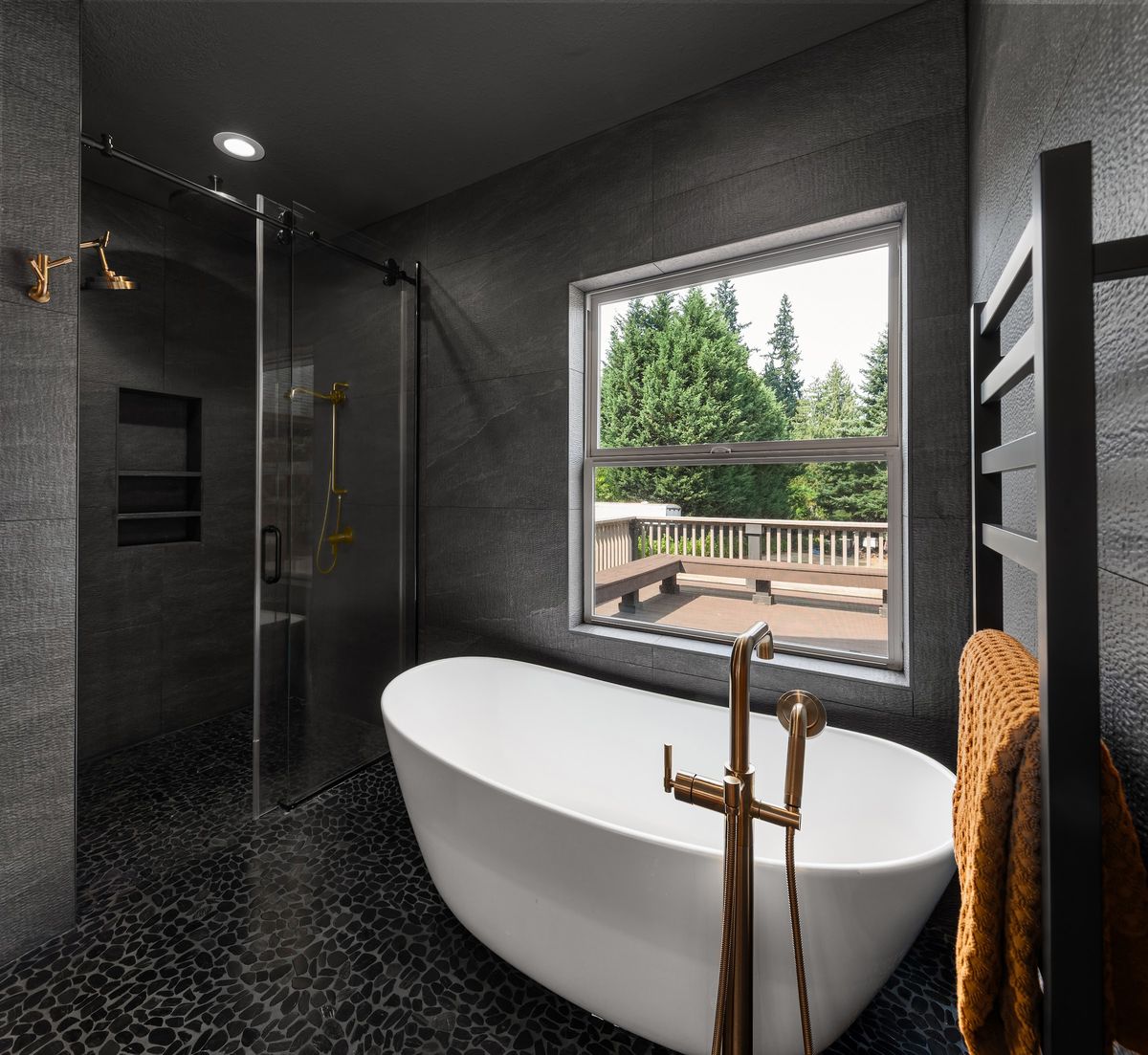 Primary bath: freestanding tub against black tile, glass shower and window onto the deck